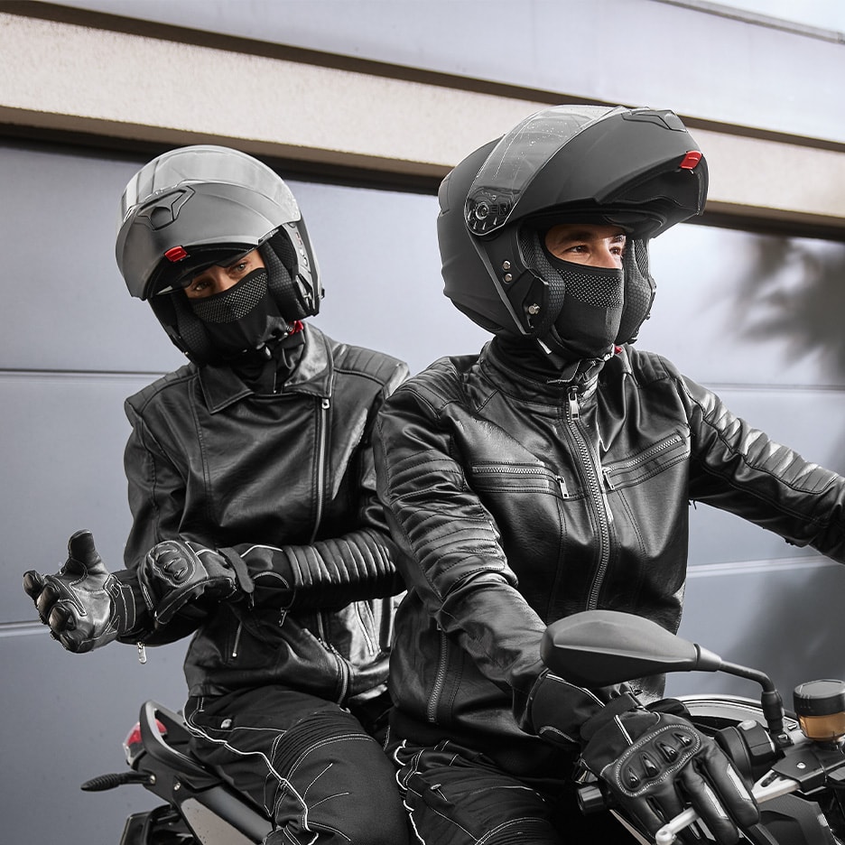 Zwei Personen in Motorradhelmen, Lederjacken und Handschuhen auf einem Motorrad.
