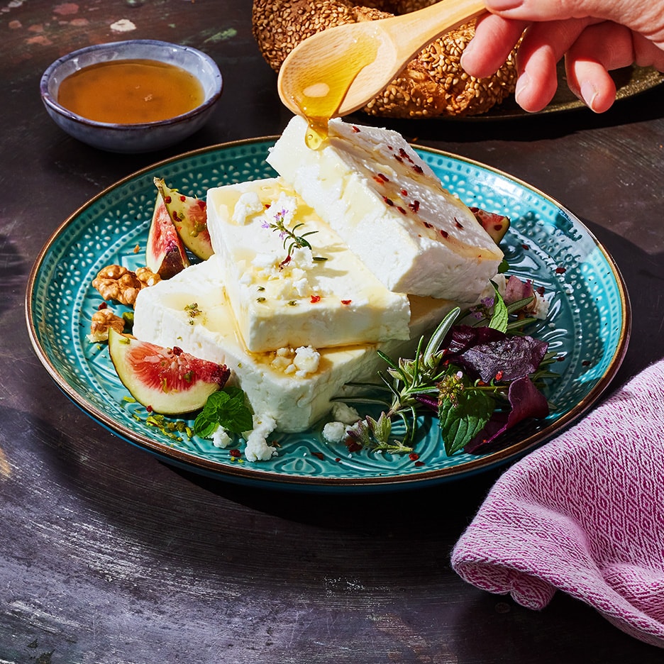 Feta mit Honig, Feigen, Walnüssen und Kräutern auf einem türkisfarbenen Teller.