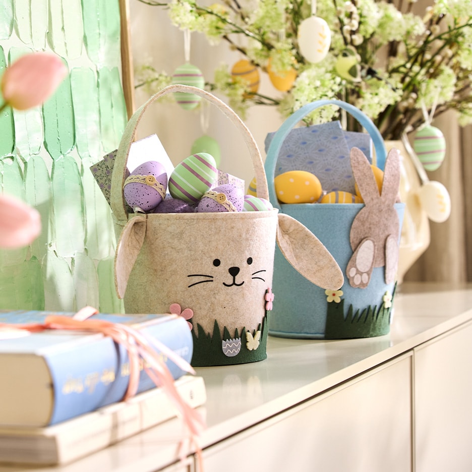 Zwei Osterkörbe in Hasenform, gefüllt mit bunten Eiern, auf einer Kommode.