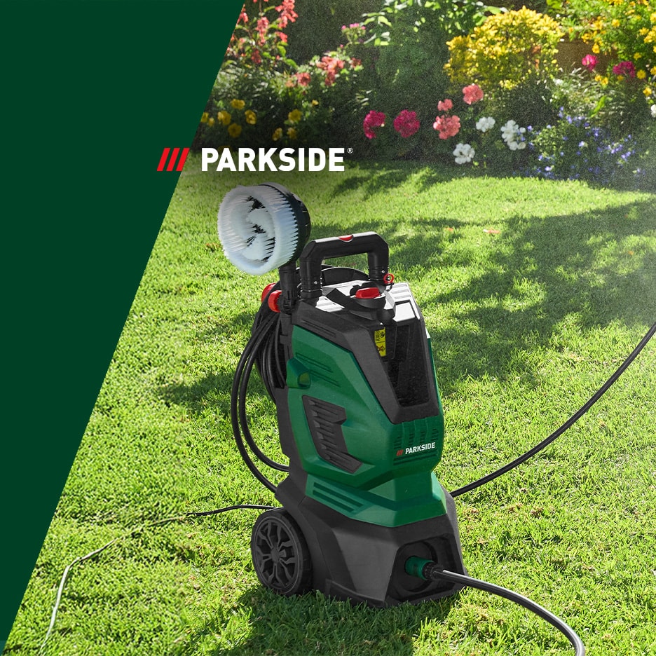 Nettoyeur haute pression vert avec brosse rotative sur une pelouse, avec des fleurs en arrière-plan.