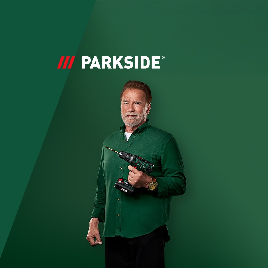 Arnold Schwarzenegger souriant, tenant une perceuse-visseuse sans fil sur fond vert.