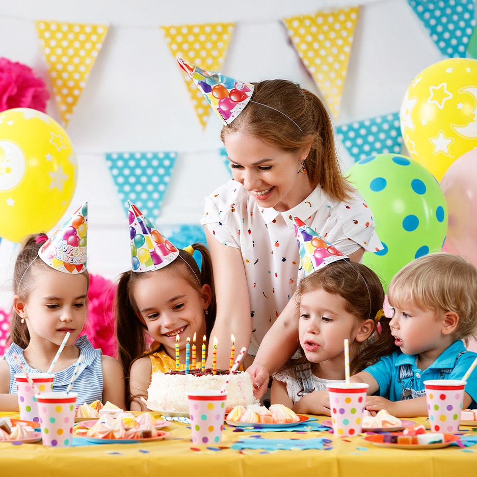 Lächelnde Kinder und Erwachsene auf einer Geburtstagsfeier mit Kuchen, Kerzen und Dekorationen.