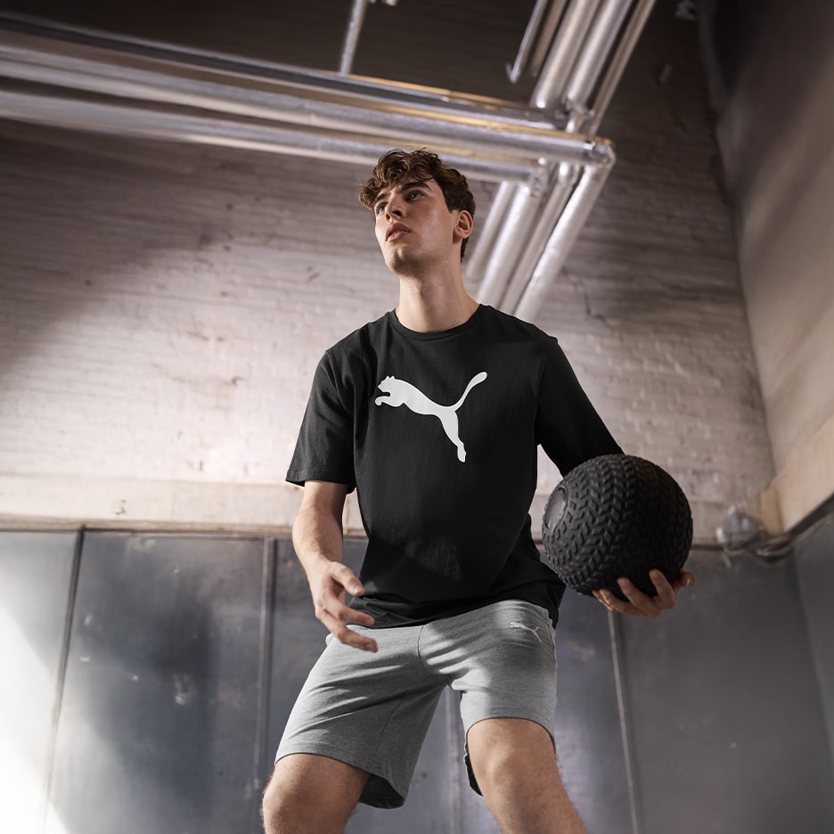 Mann in schwarzem T-Shirt und grauen Shorts hält einen Medizinball.