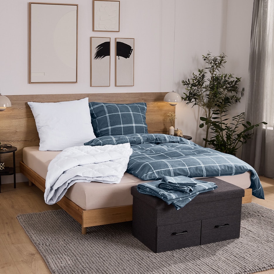 Schlafzimmer mit Holzbett, blauer karierter Bettwäsche und Aufbewahrungsbox.