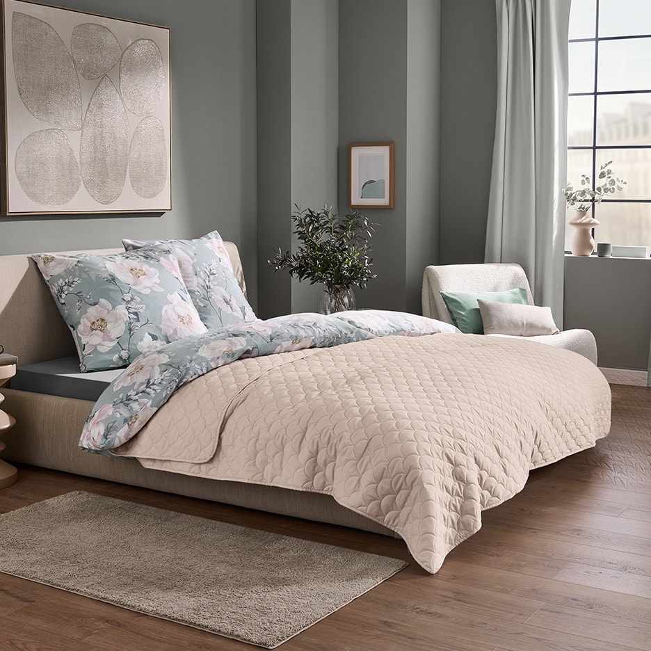 Schlafzimmer mit einem Bett mit floralem Bettbezug und einer gesteppten beigen Tagesdecke.