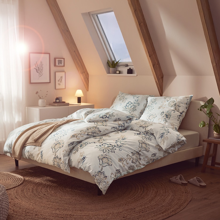 Dachschlafzimmer mit Doppelbett, Bettwäsche mit Blumenmuster, Nachttisch und Dachfenster.
