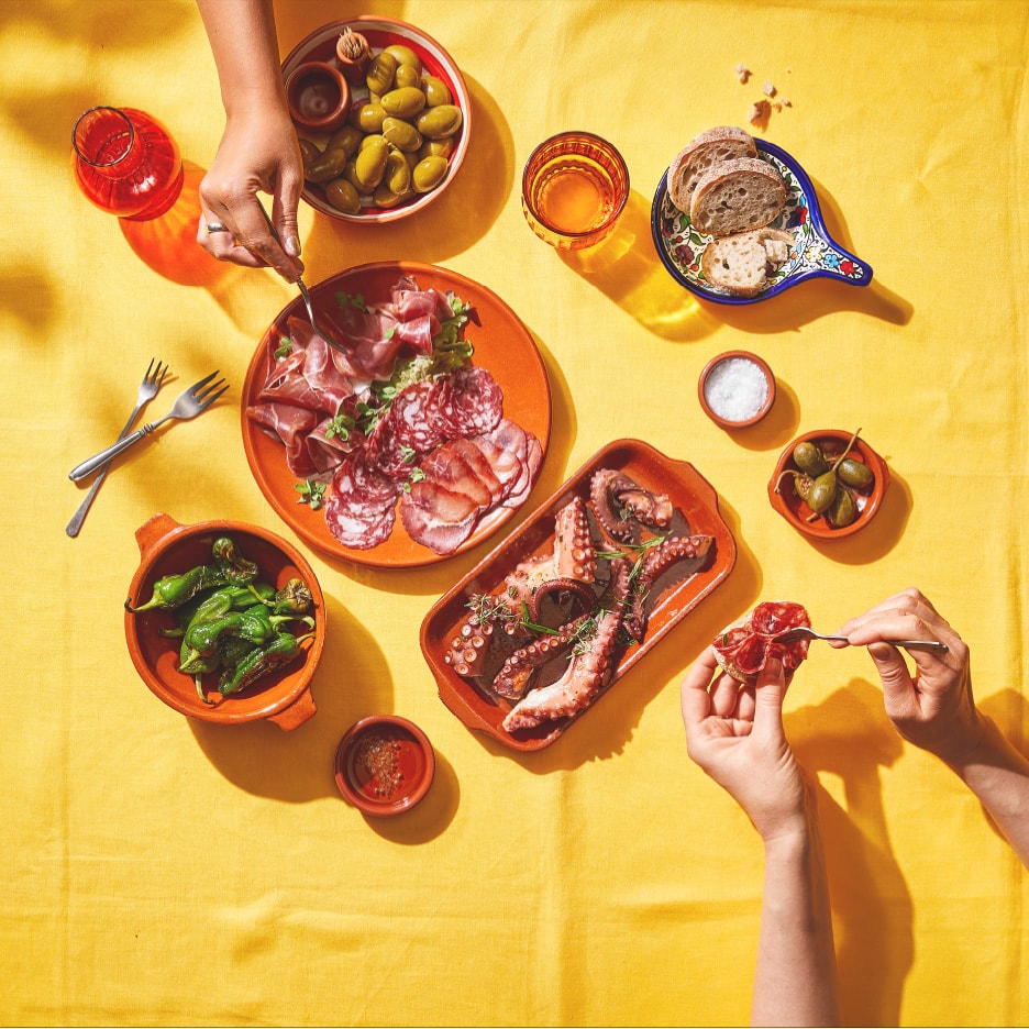 Aufsicht auf eine Tapas-Auslage mit Wurstwaren, Oktopus, Oliven und Paprika.
