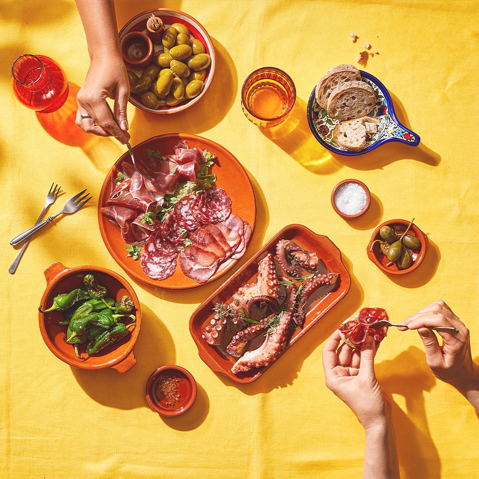 Spanische Tapas mit Oktopus, Wurstwaren, Oliven, Paprika und Brot auf gelbem Tisch.