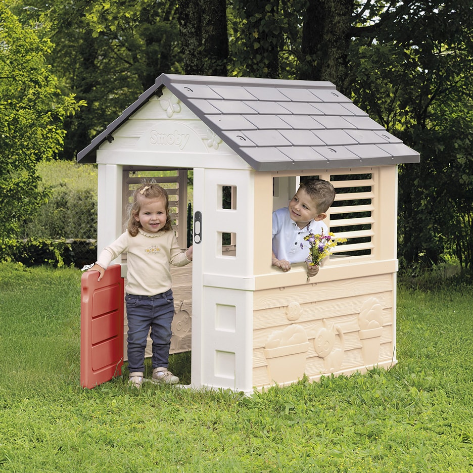 Zwei Kinder spielen in einem Garten-Spielhaus aus Kunststoff, eines hält einen Blumenstrauß.