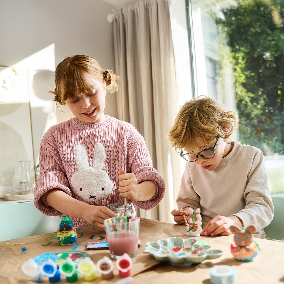 Zwei Kinder bemalen Osterfiguren und bunte Eier mit Acrylfarben.