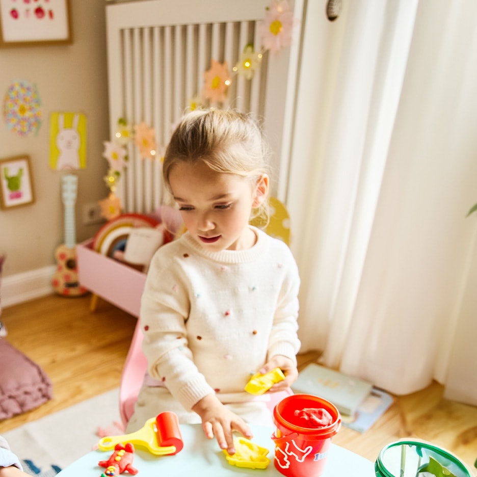 Mädchen spielt mit Knete und Förmchen an einem hellblauen Tisch.