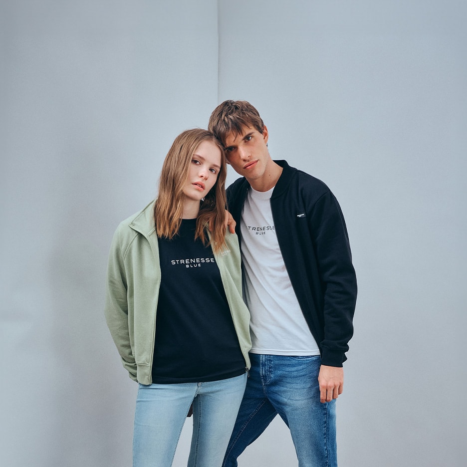 Paar in Sweatshirts und Jeans, mit minimalistischen Schriftzügen auf den Oberteilen.