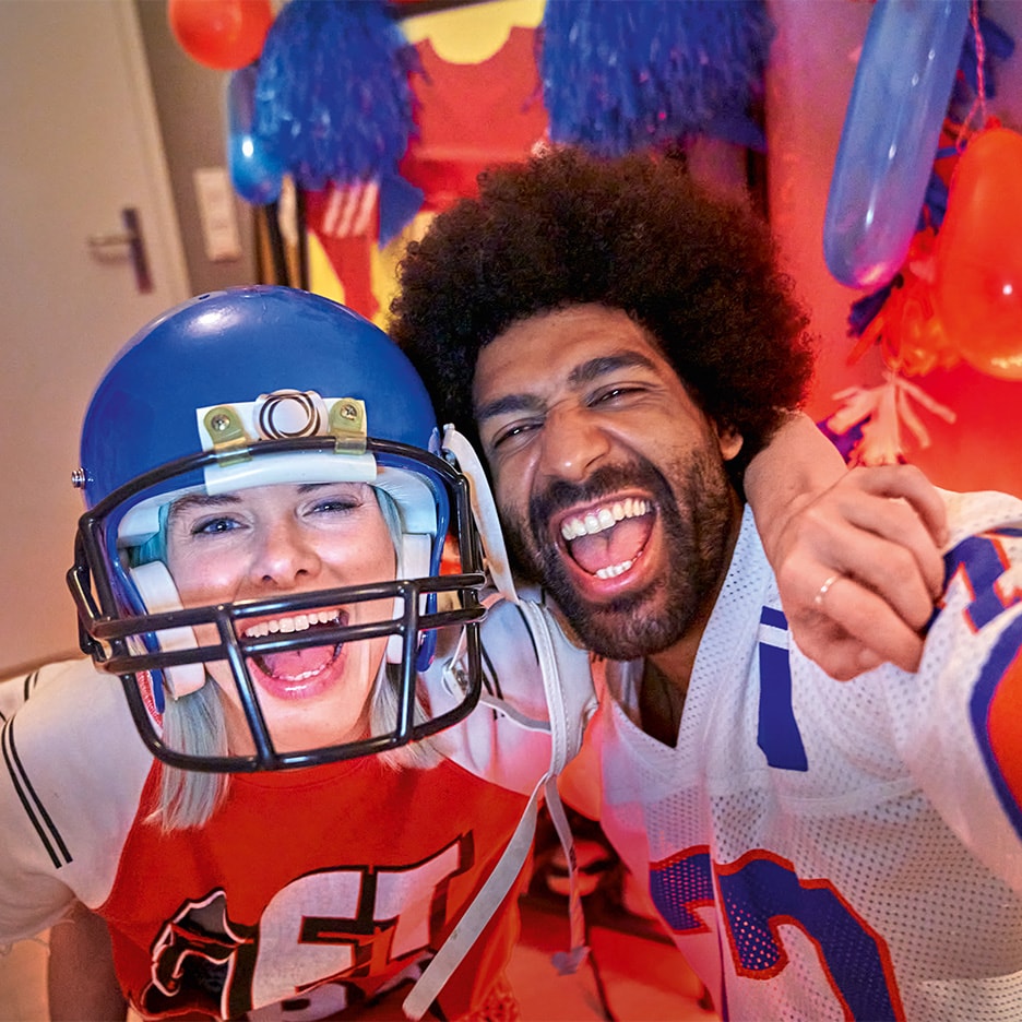 Zwei lachende Freunde in American-Football-Trikots und Helm, die feiern.