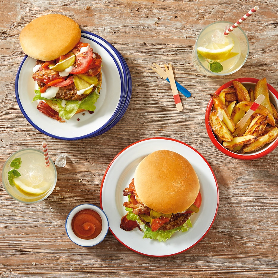 Zwei Burger mit Pommes Frites und Limonade auf einem Holztisch.