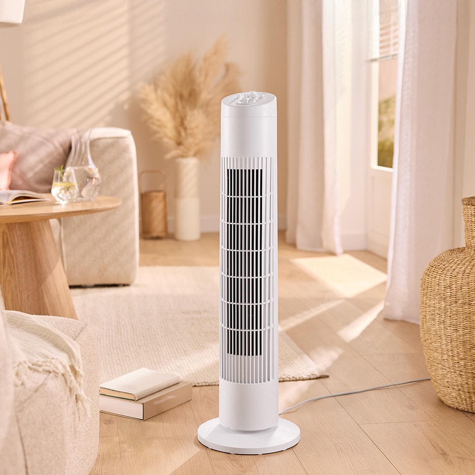 Weißer Turmventilator in einem hellen Wohnzimmer mit Sofa und Pampasgras.