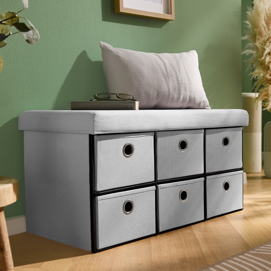 Sitzbank mit sechs grauen Stoffschubladen und einem Kissen in einem Wohnzimmer.