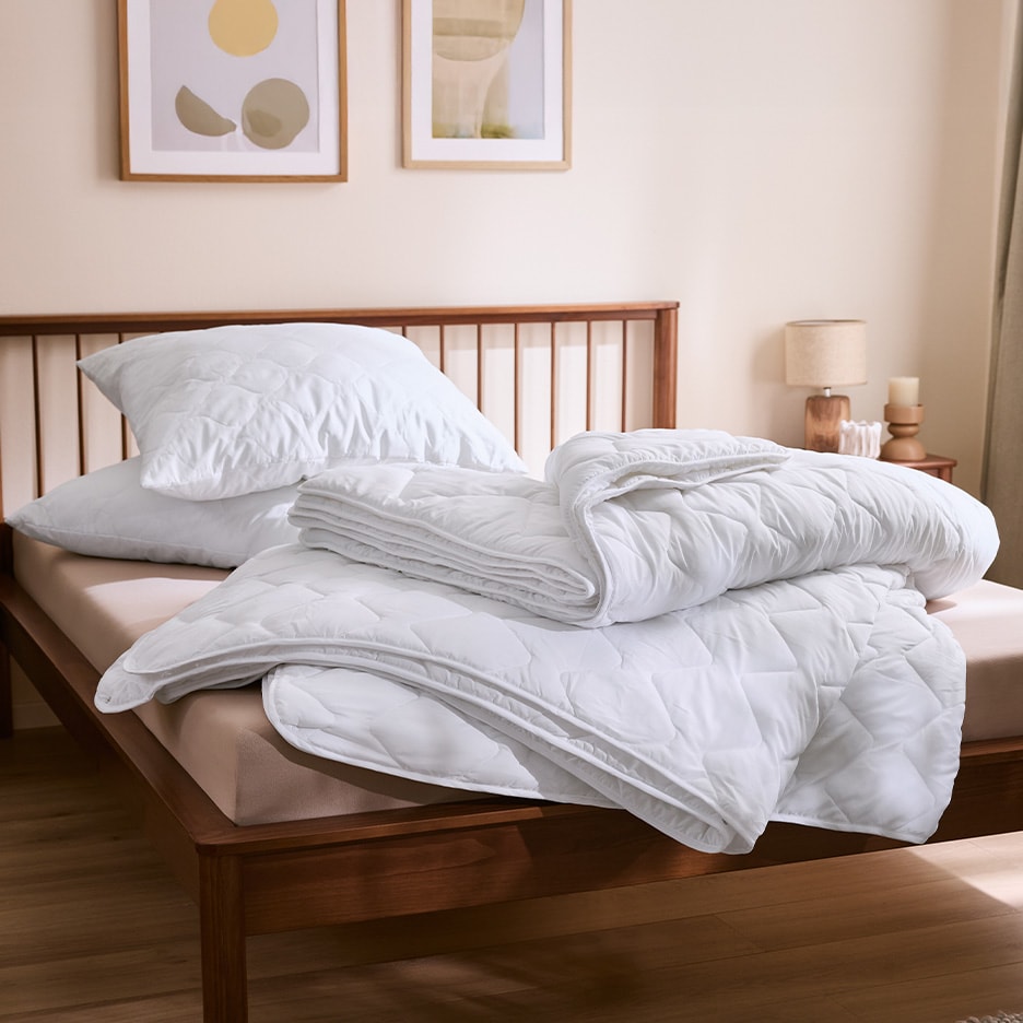 Gesteppte weiße Bettdecken und Kissen auf einem Holzbett in einem gemütlichen Schlafzimmer.