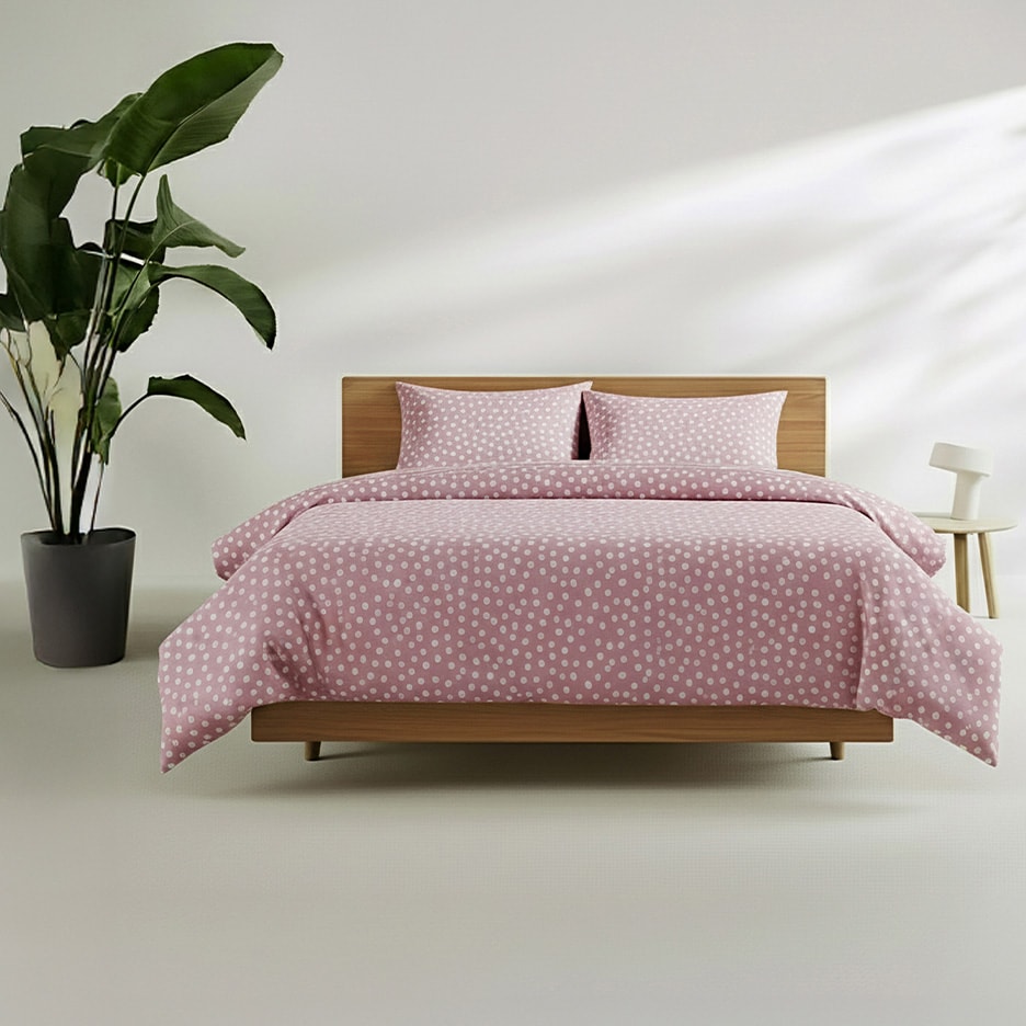 Bett mit rosa Bettwäsche mit weißen Punkten, grüner Pflanze und Nachttisch mit Lampe.