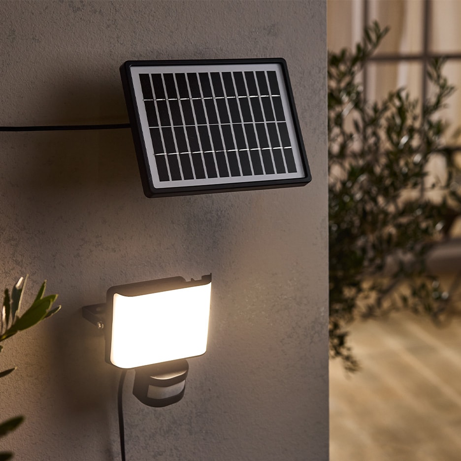 Solar-LED-Strahler mit Bewegungssensor an einer grauen Wand montiert.