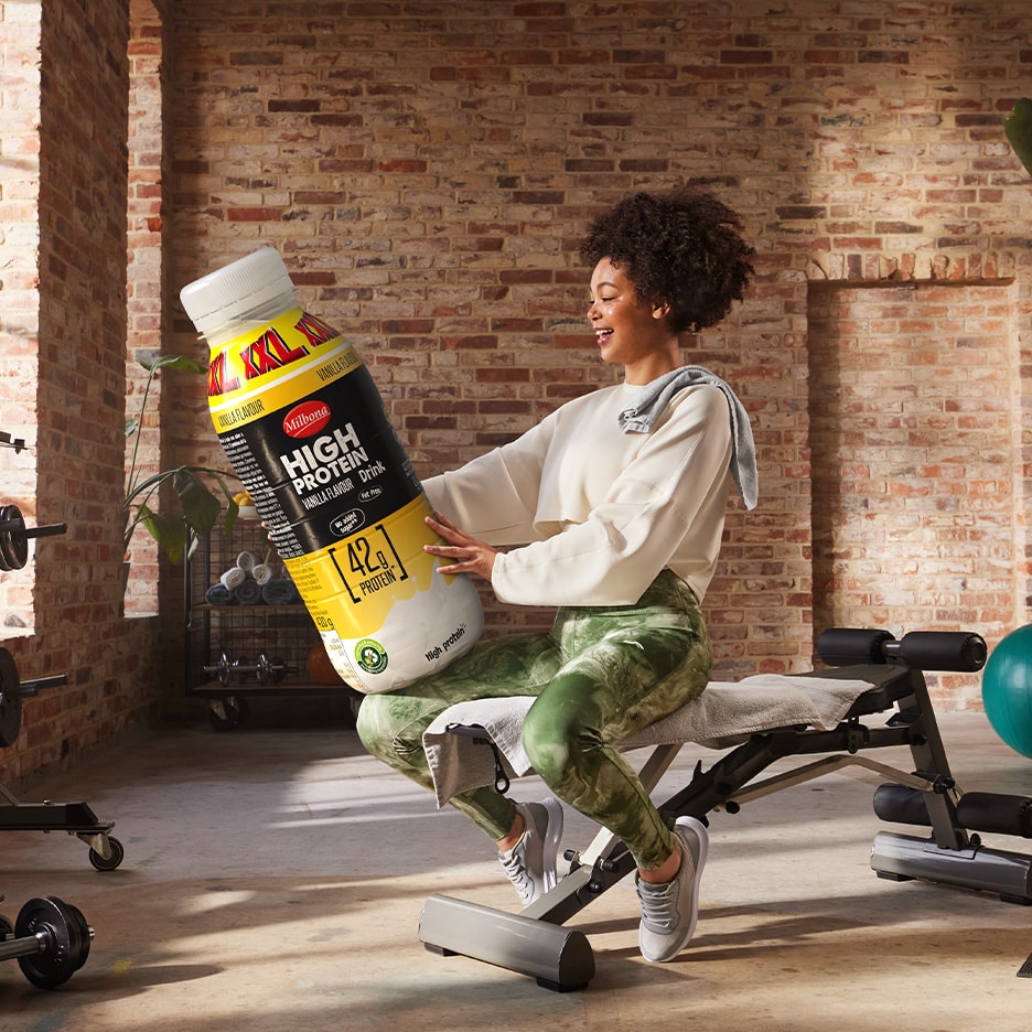 Frau hält einen riesigen Milbona High Protein Vanille-Drink in einem Fitnessstudio.