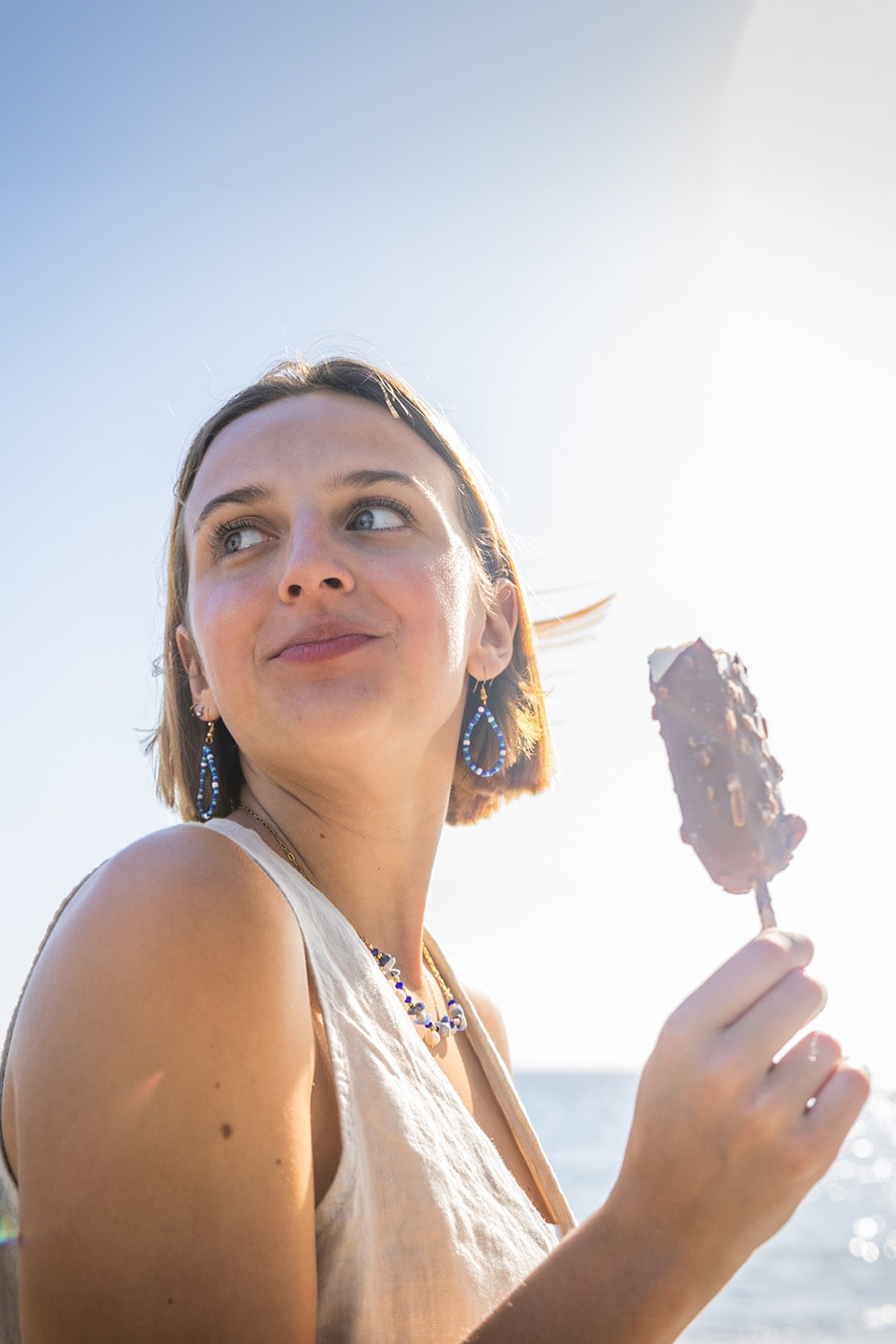 Frau mit Eis am Stiel und blauen Ohrringen am Meer.