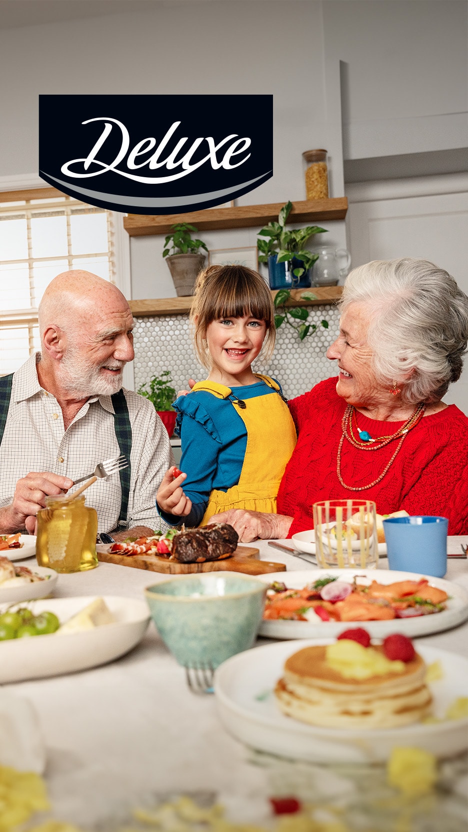 Famiglia sorridente a tavola con piatti festivi, logo 'Deluxe'.