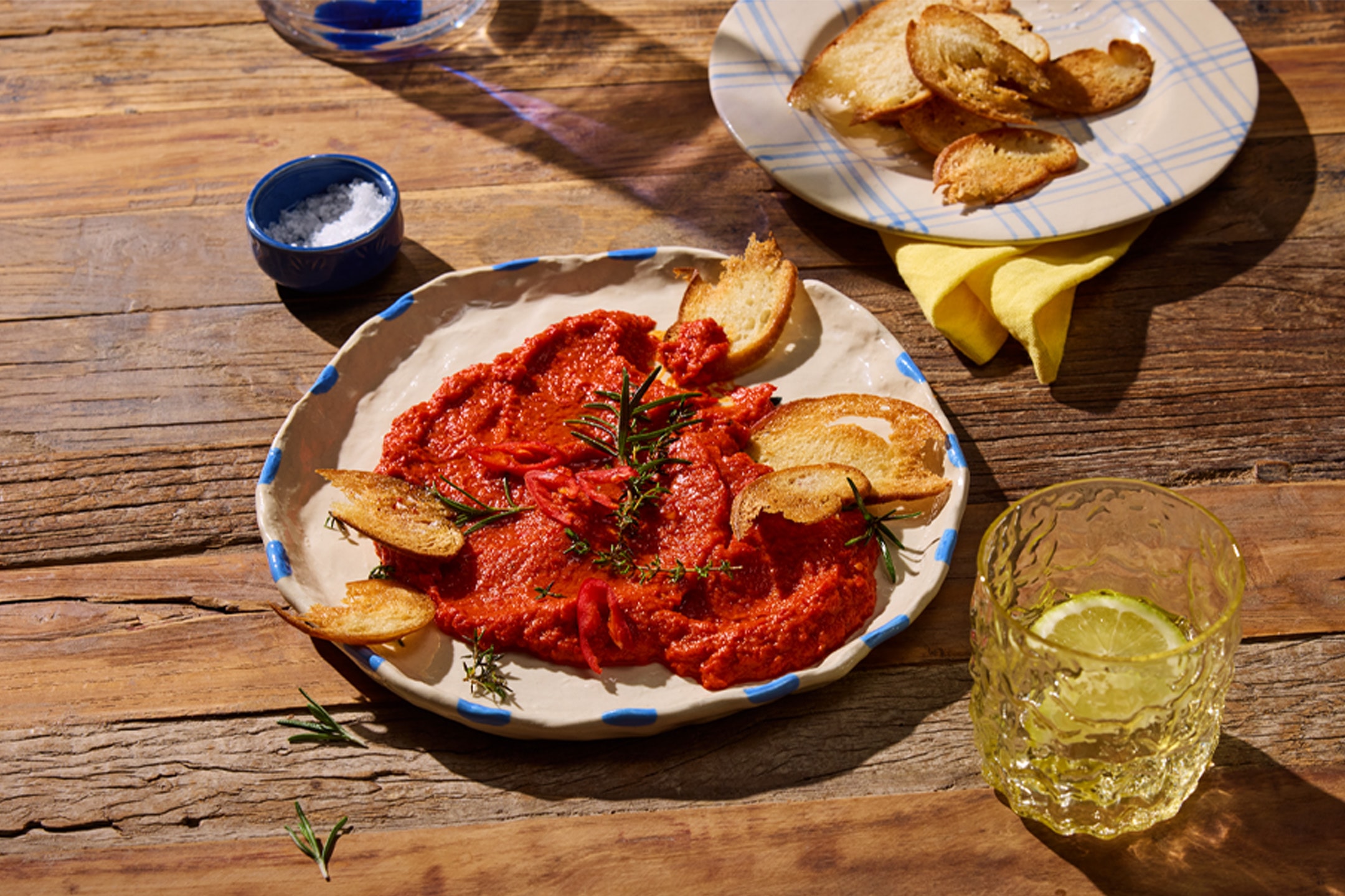 Rote Pastete mit Crostini, Rosmarin und einem Glas Limonade auf einem Holztisch.