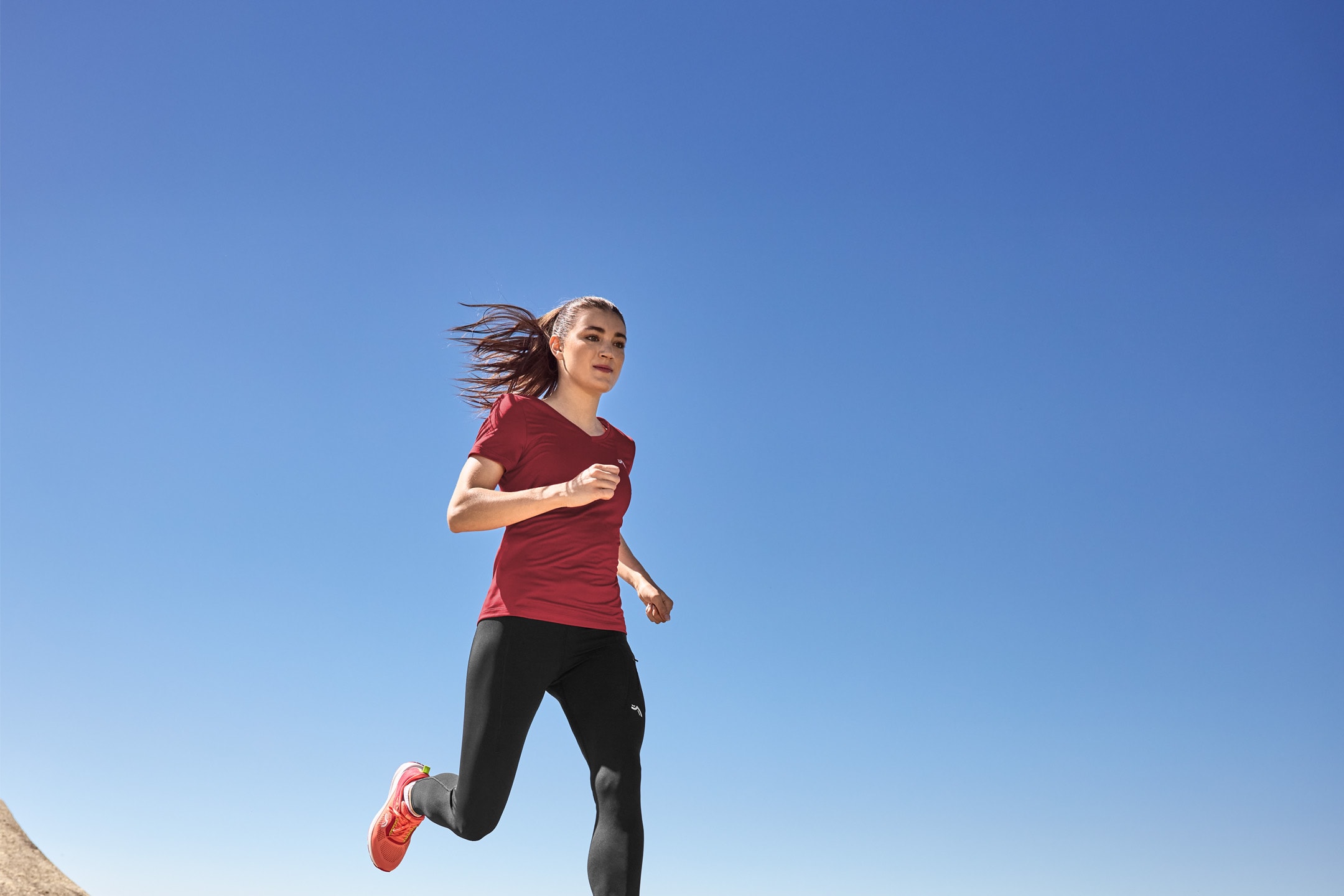 Frau läuft draußen in rotem Sport-T-Shirt, schwarzen Leggings und Laufschuhen.