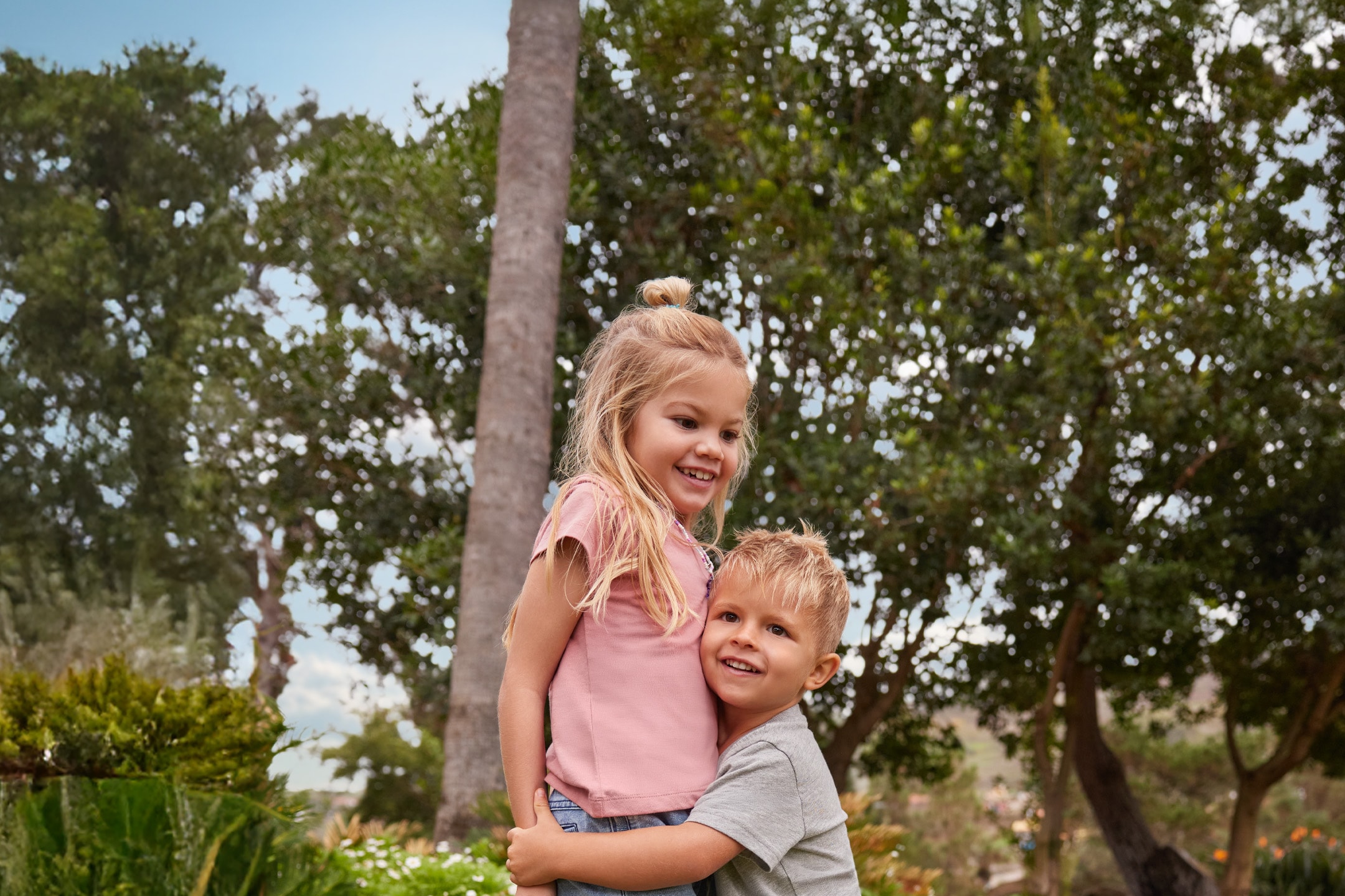 Zwei lächelnde Kinder, ein Mädchen und ein Junge, umarmen sich im Freien.
