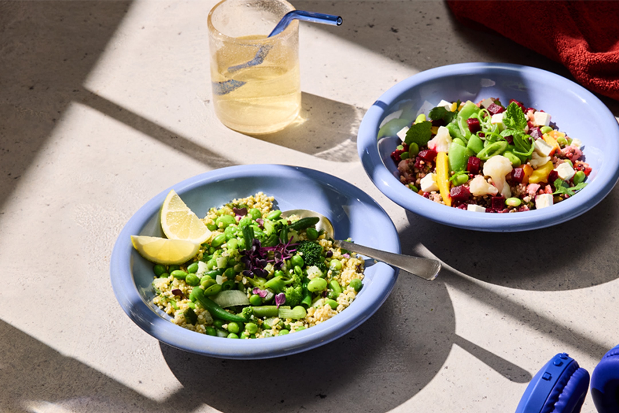 Deux bols de salade colorés avec des légumes frais et des céréales, un verre d'eau et des écouteurs.