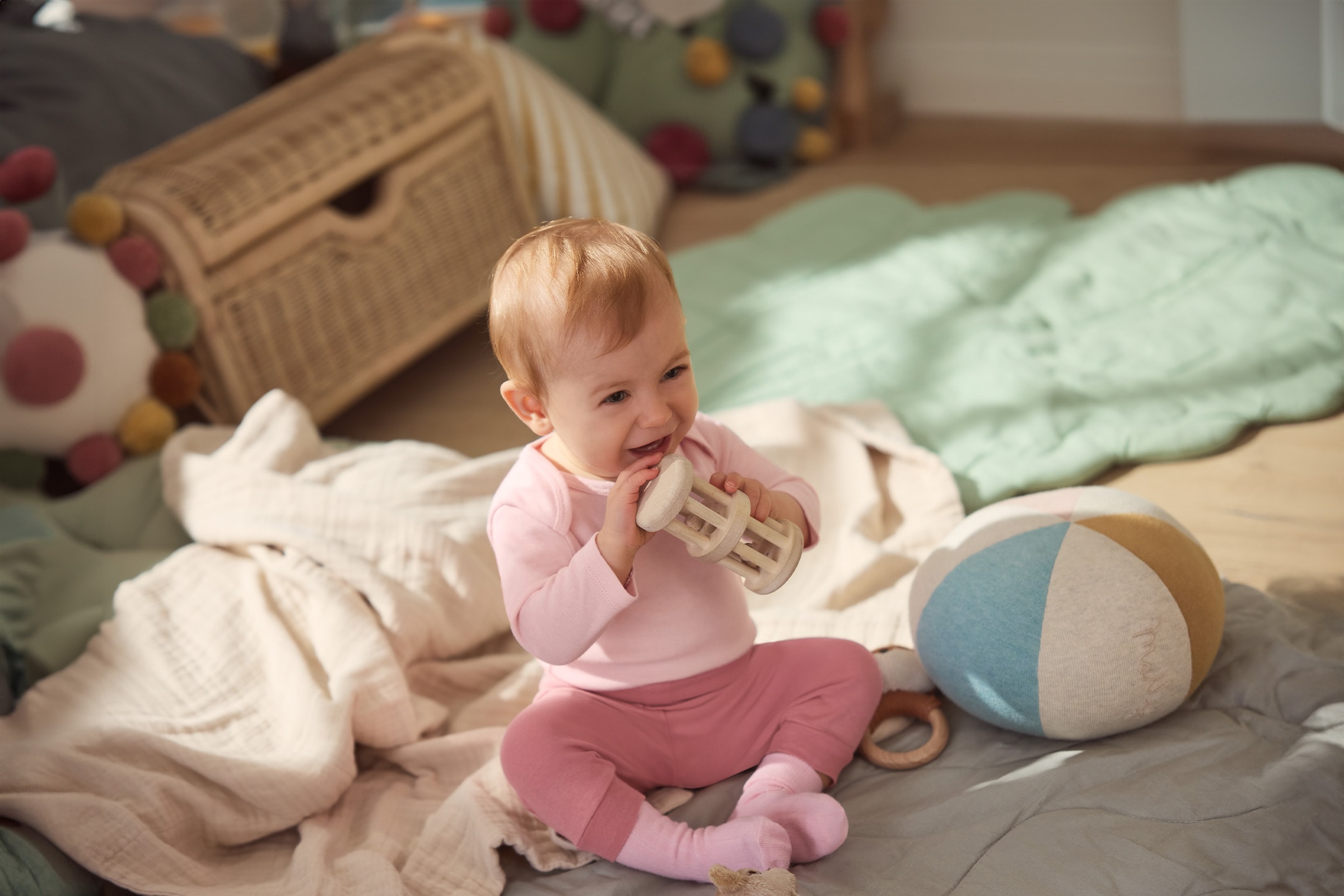 Baby in rosa Kleidung spielt mit Holzrassel auf Decken