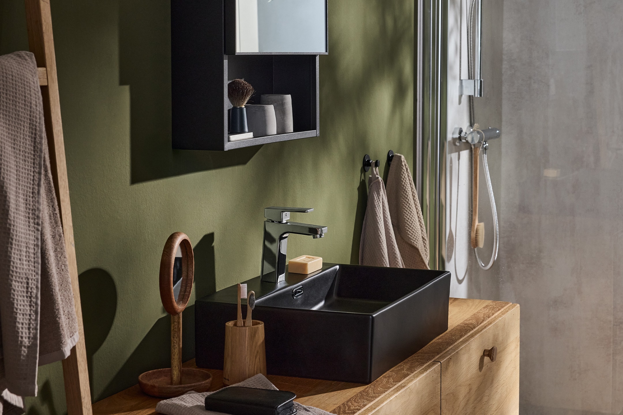 Modernes Badezimmer mit schwarzem Waschbecken, Chromarmatur, Holzunterschrank und grüner Wand.