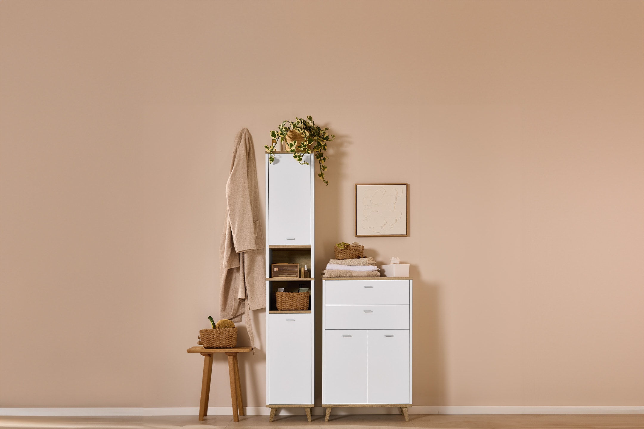 Weiße und holzfarbene Badmöbel mit Bademantel, Hocker und Pflanzen.
