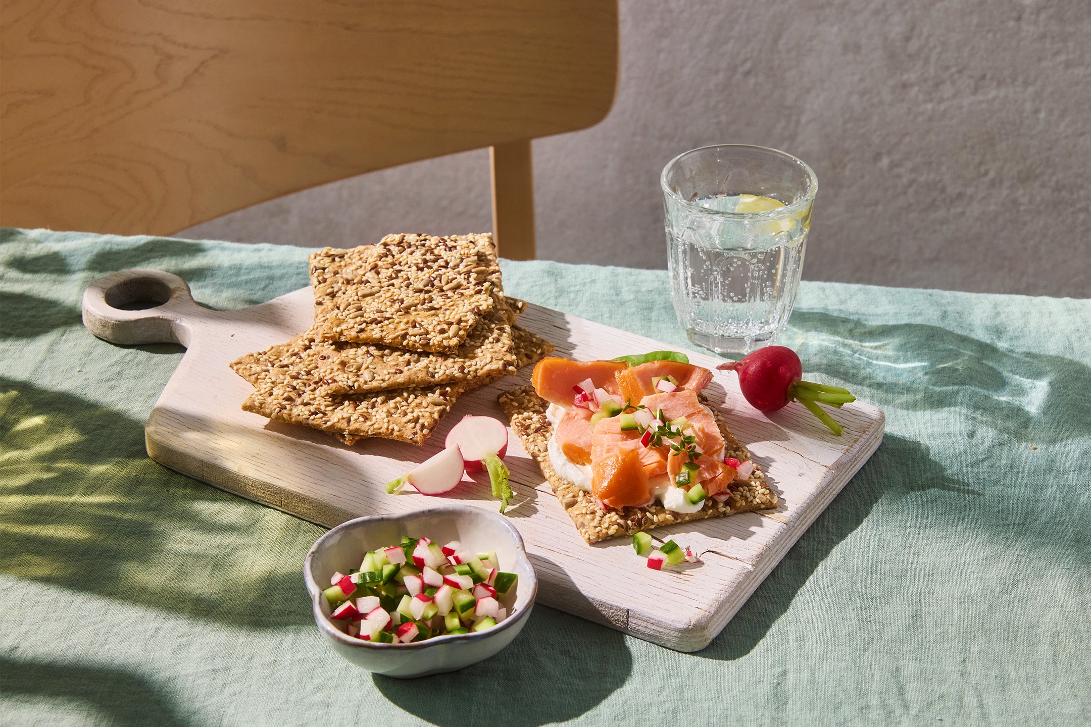 Crackers aux graines avec du saumon fumé, du fromage frais et des radis sur une planche en bois.