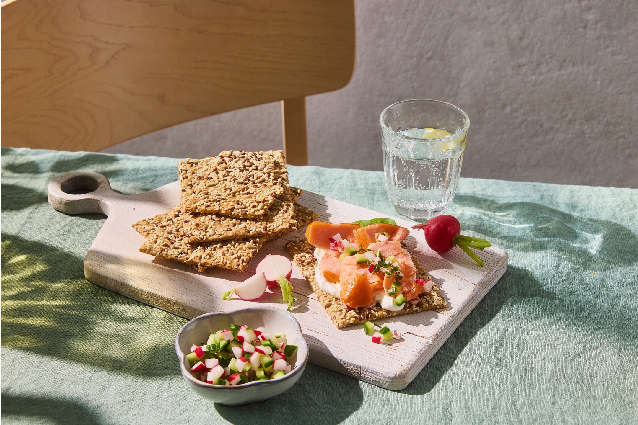Samen-Cracker mit Räucherlachs, Frischkäse und Radieschen auf einem Schneidebrett.