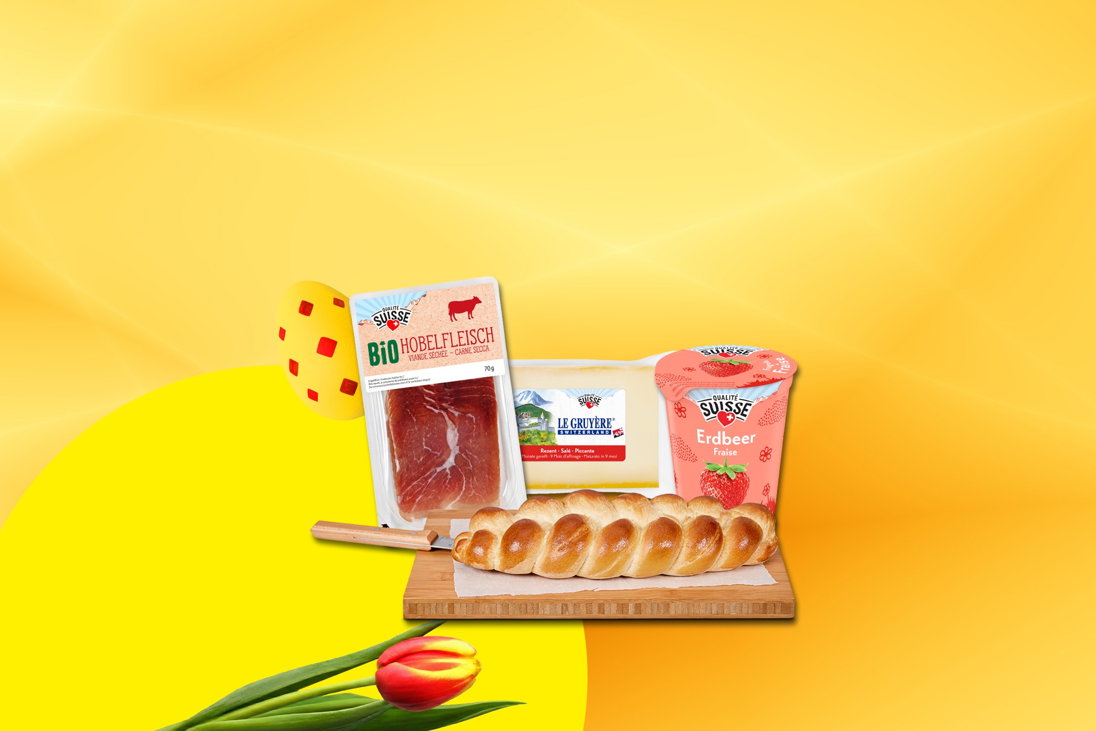 Viande séchée, fromage Gruyère, yaourt à la fraise et tresse de pain sur une planche à découper, avec des tulipes et des œufs de Pâques.