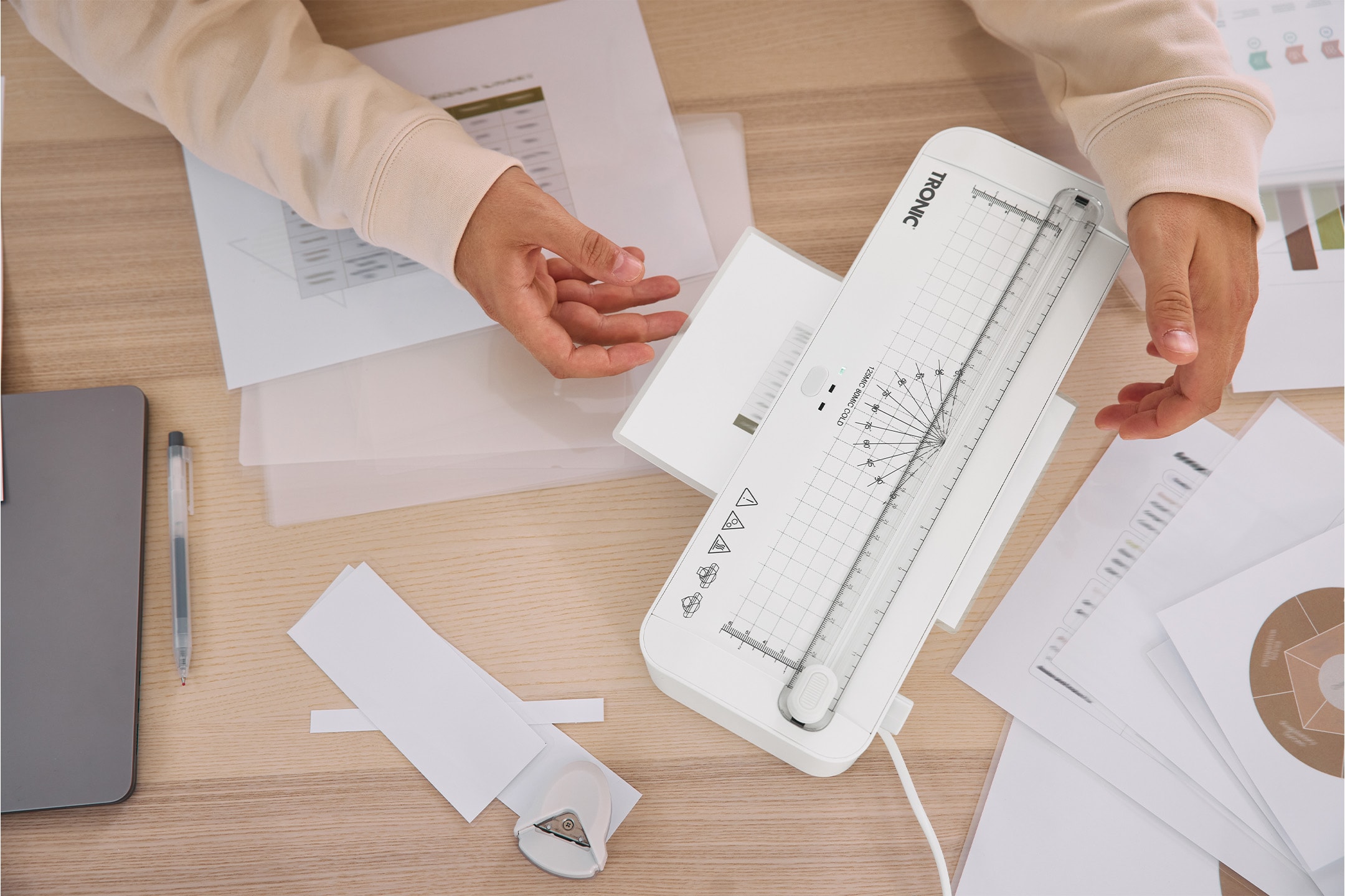 Person laminiert Dokumente mit einem TRONIC Laminiergerät auf einem Holztisch.