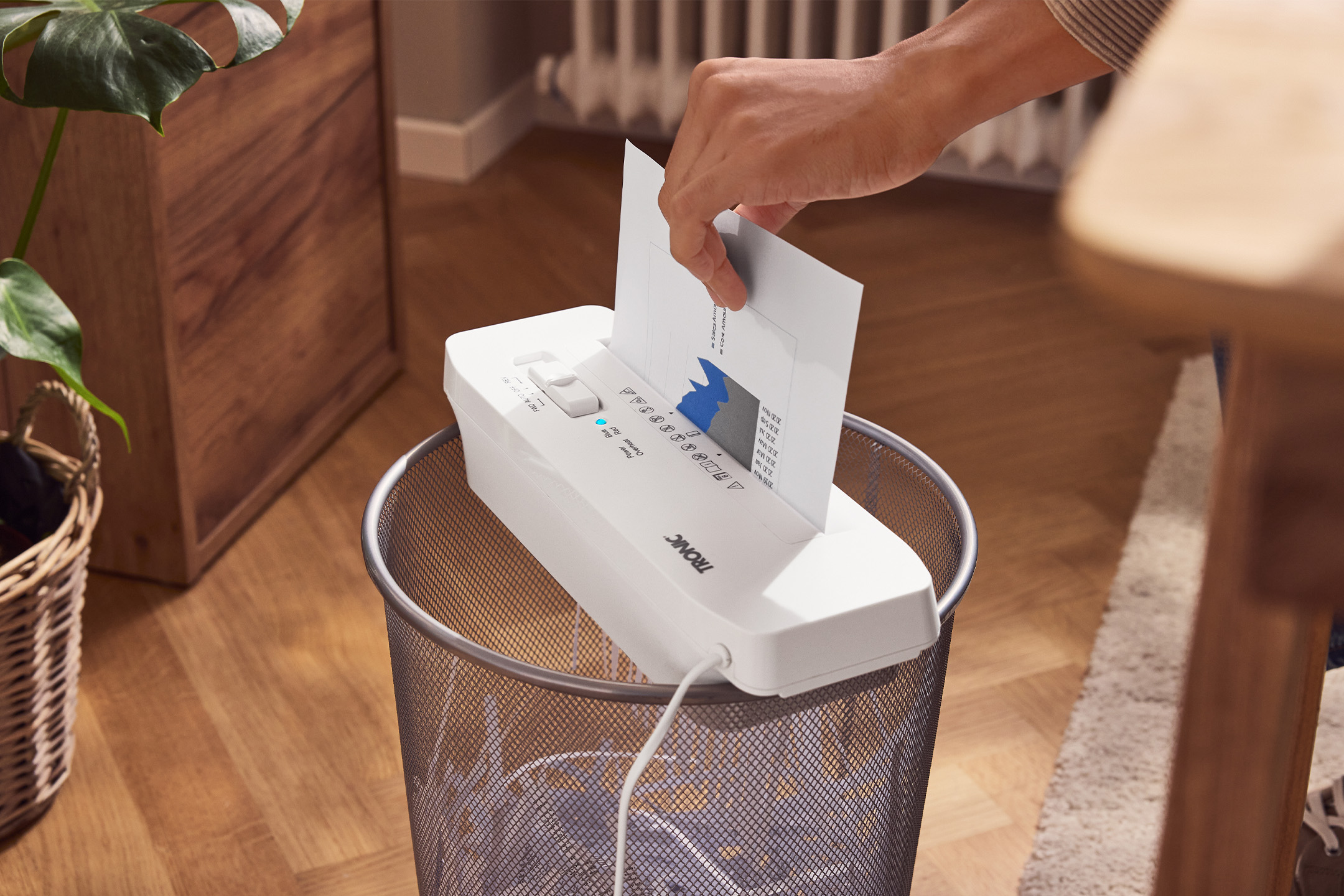 Eine Person schreddert ein Dokument mit einem TRONIC Aktenvernichter über einem Mülleimer.