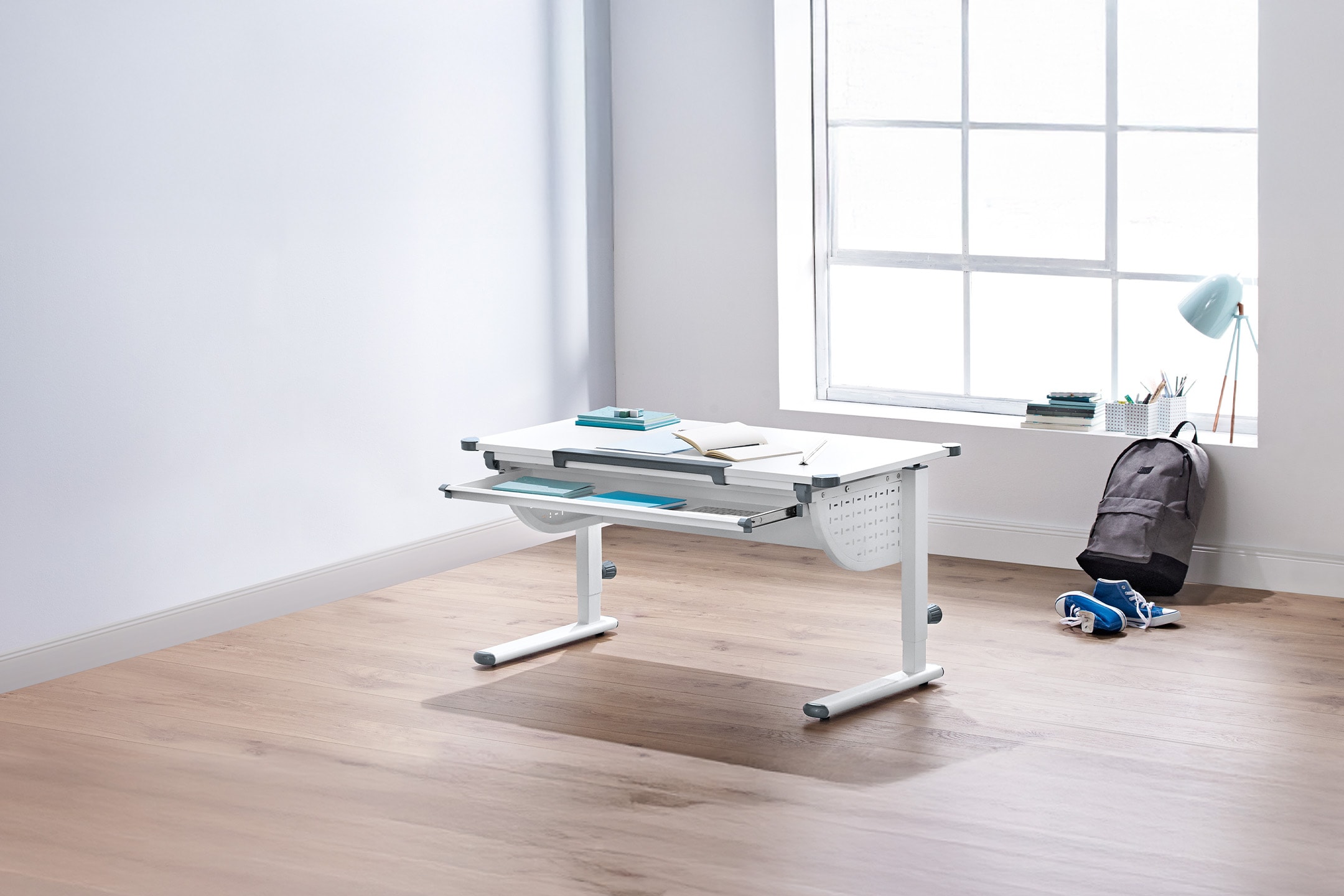 Weißer höhenverstellbarer Schreibtisch mit Auszugsschublade, Rucksack und Turnschuhen.