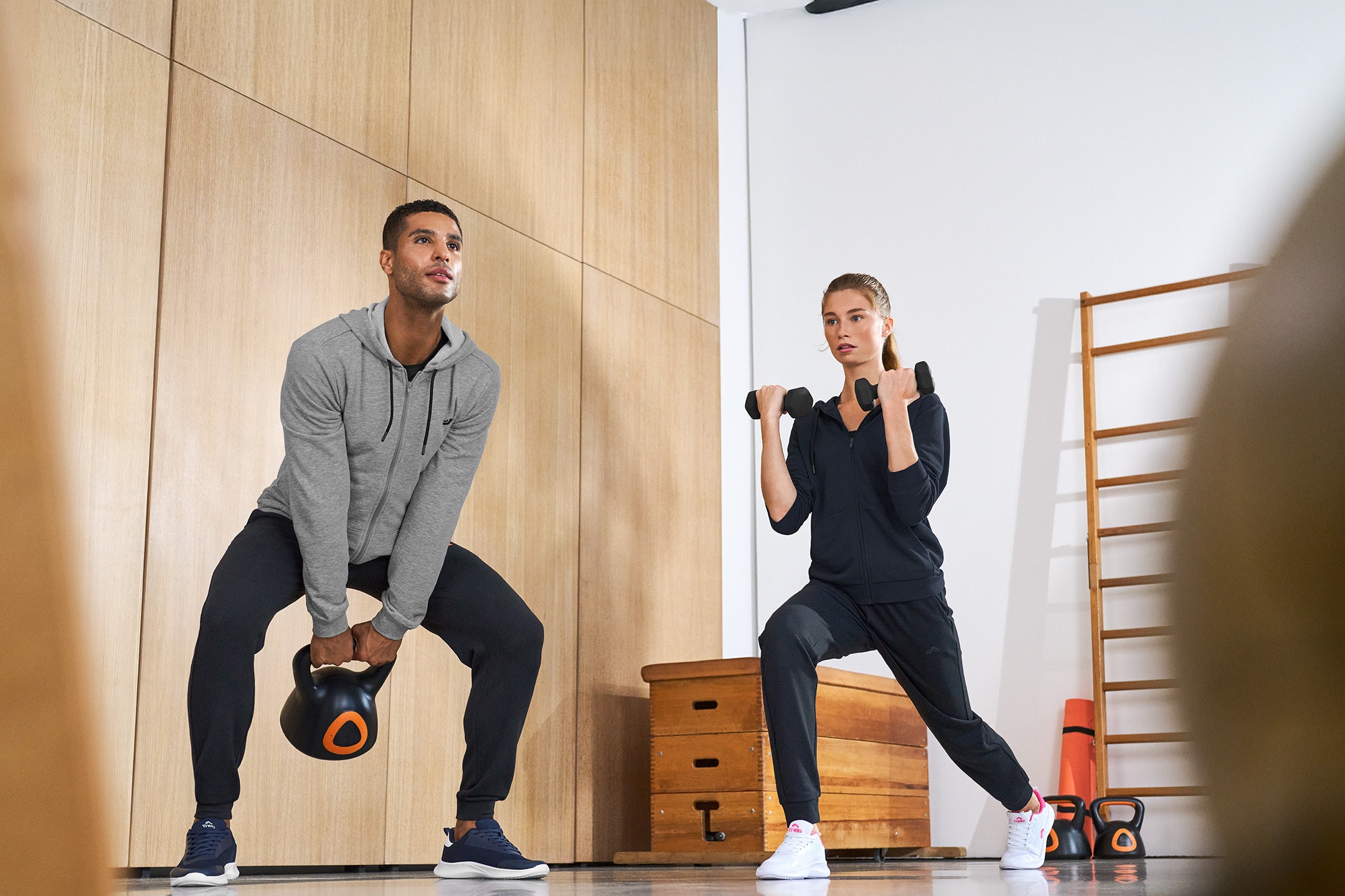 Mann mit Kettlebell und Frau mit Hanteln beim Training in Sportbekleidung.