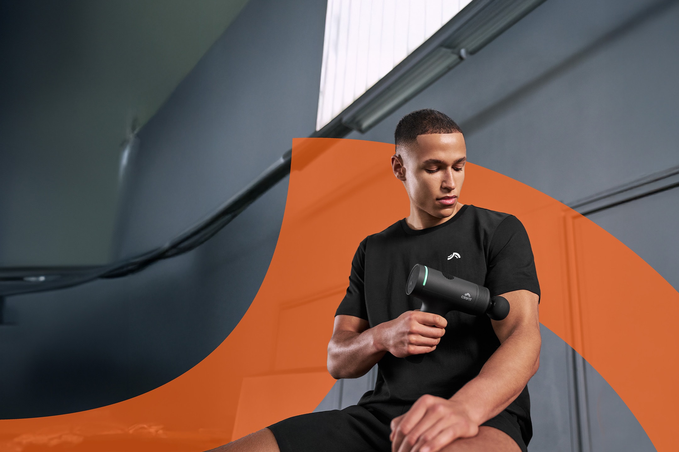 Ein Mann benutzt eine Massagepistole an seinem Arm und trägt schwarze Sportkleidung.