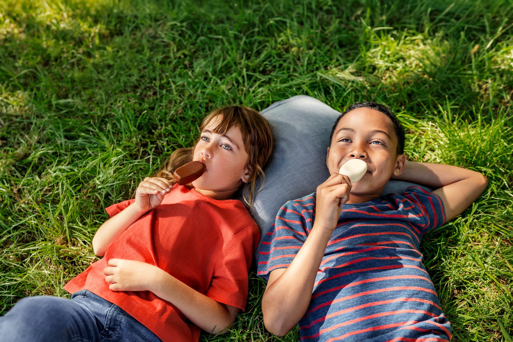 Zwei Kinder essen Eiscreme, während sie an einem sonnigen Tag auf dem Gras liegen.