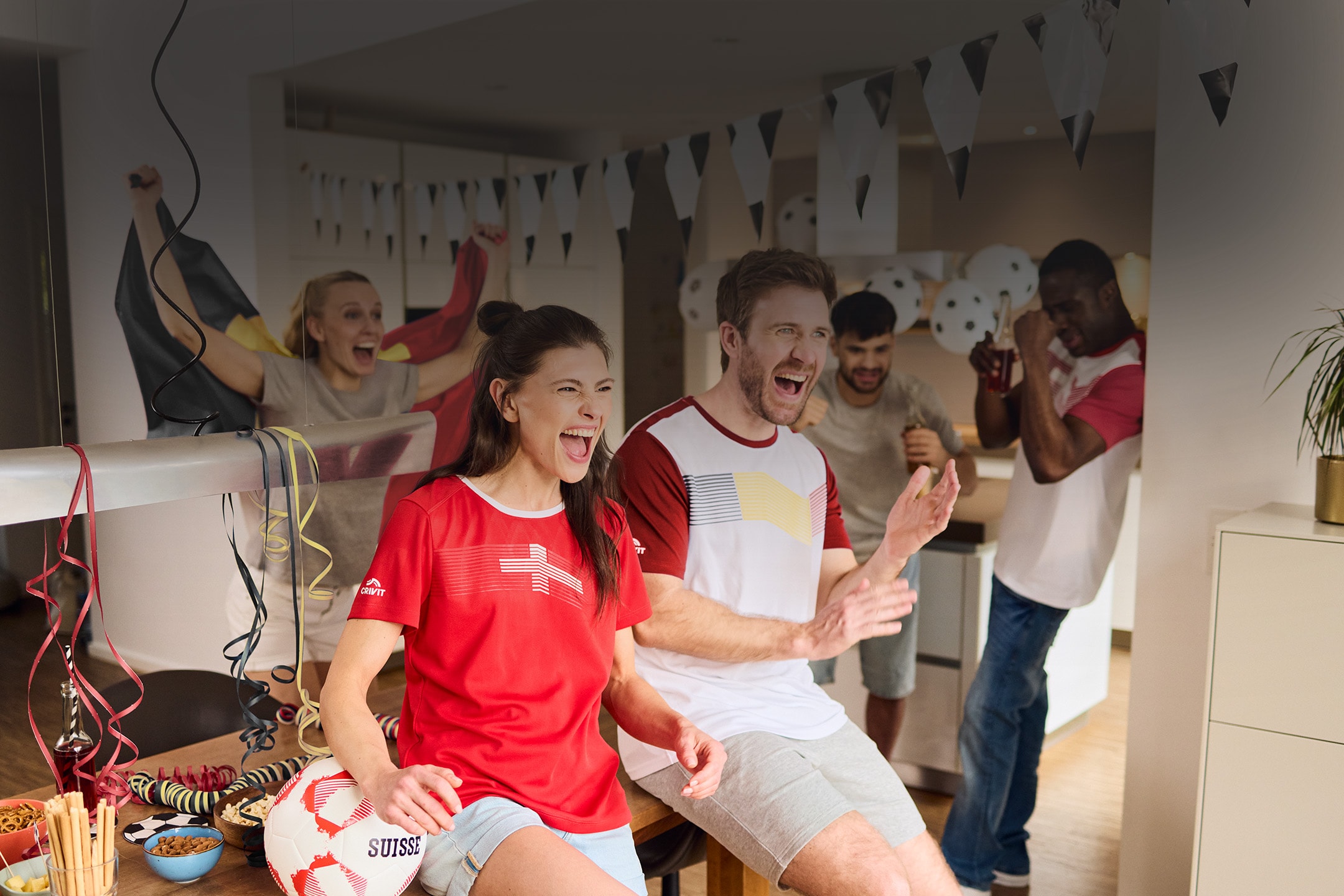 Begeisterte Freunde in Sport-Fan-Shirts schauen ein Fußballspiel, mit Snacks und einem Fußball.