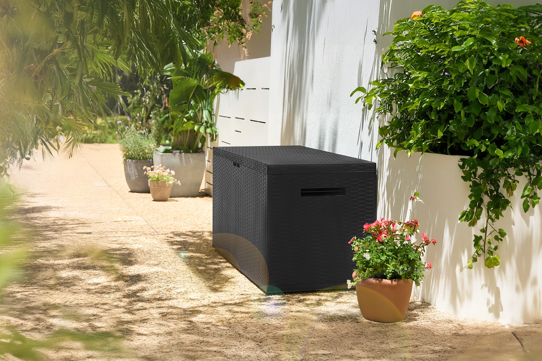 Schwarze Outdoor-Aufbewahrungsbox auf einer Terrasse mit Topfpflanzen und Sonnenlicht.