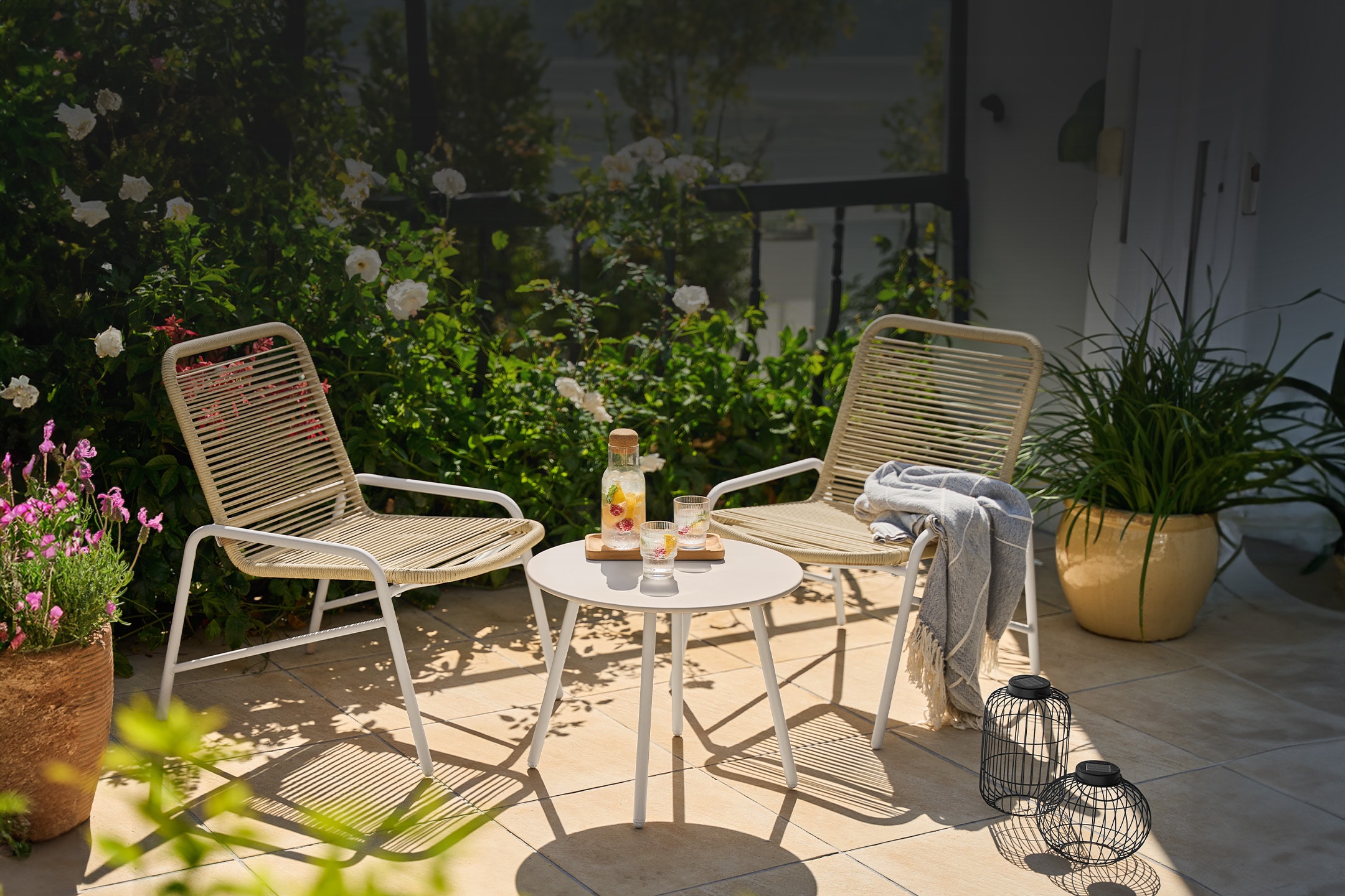 Due sedie da giardino e un tavolino con bevande su un patio soleggiato.