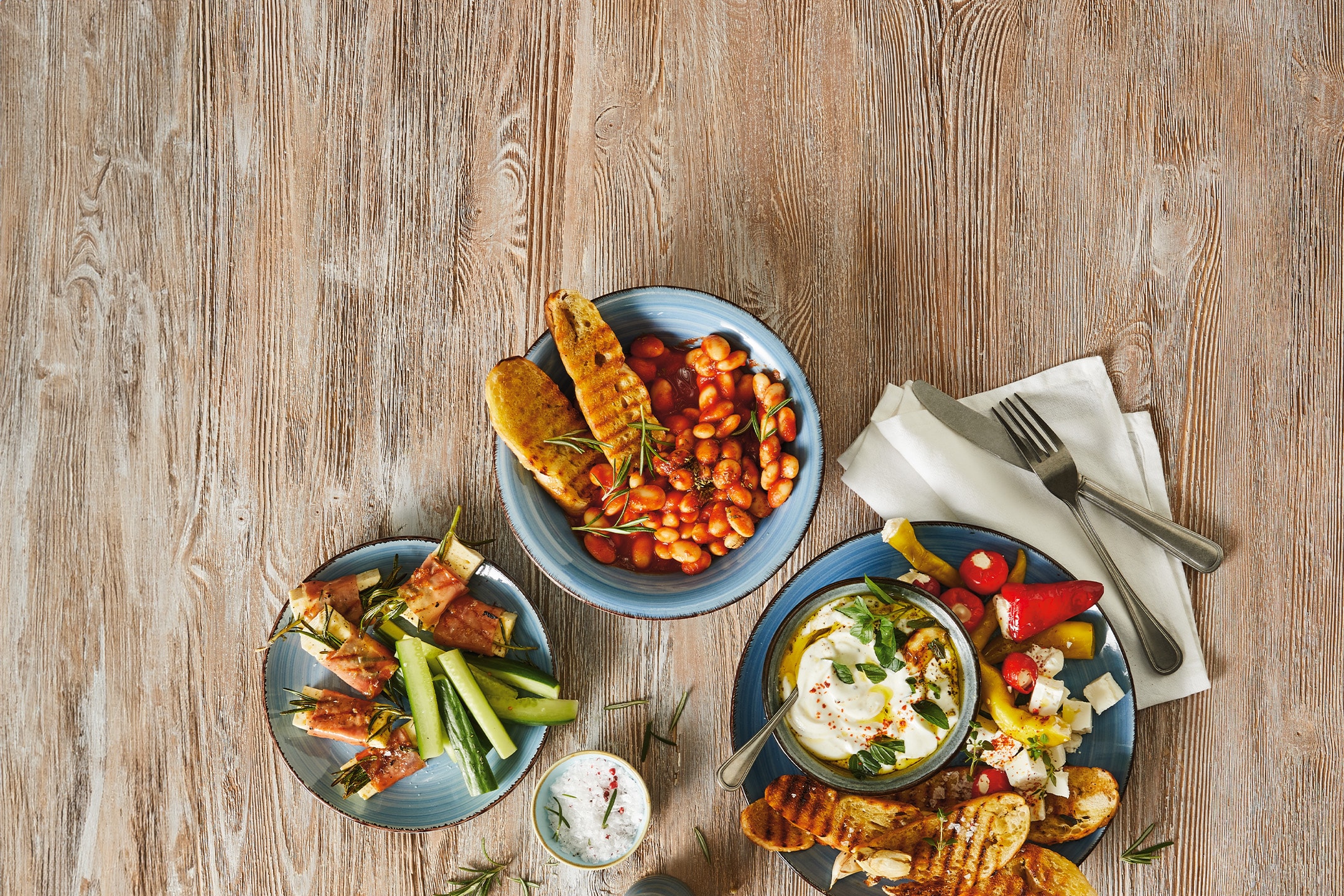 Gebackene Bohnen, Schinken-Gurken-Röllchen und eine Schale Frischkäse mit geröstetem Brot.