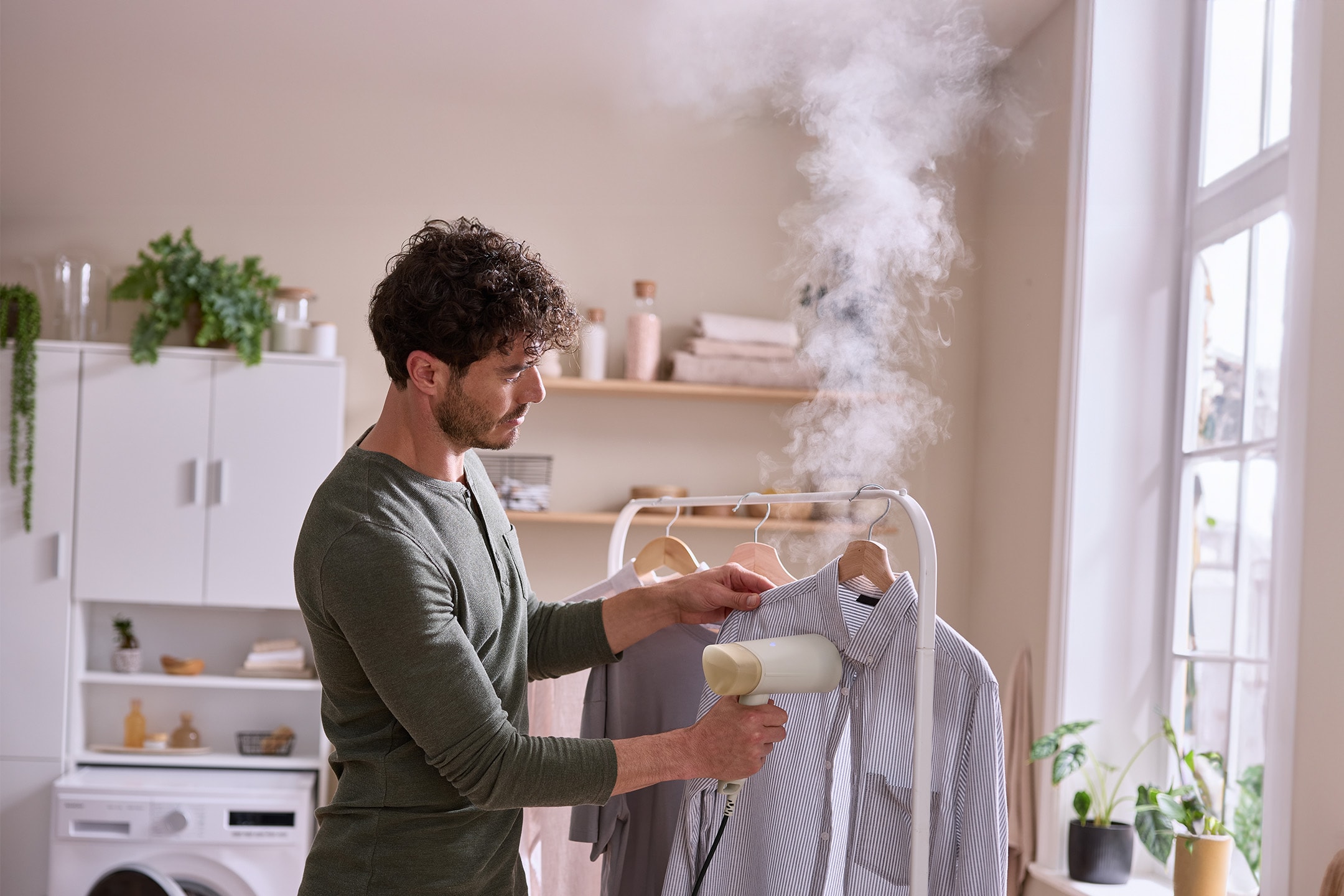Mann bügelt Hemd mit Dampfglätter in einem hellen Raum.