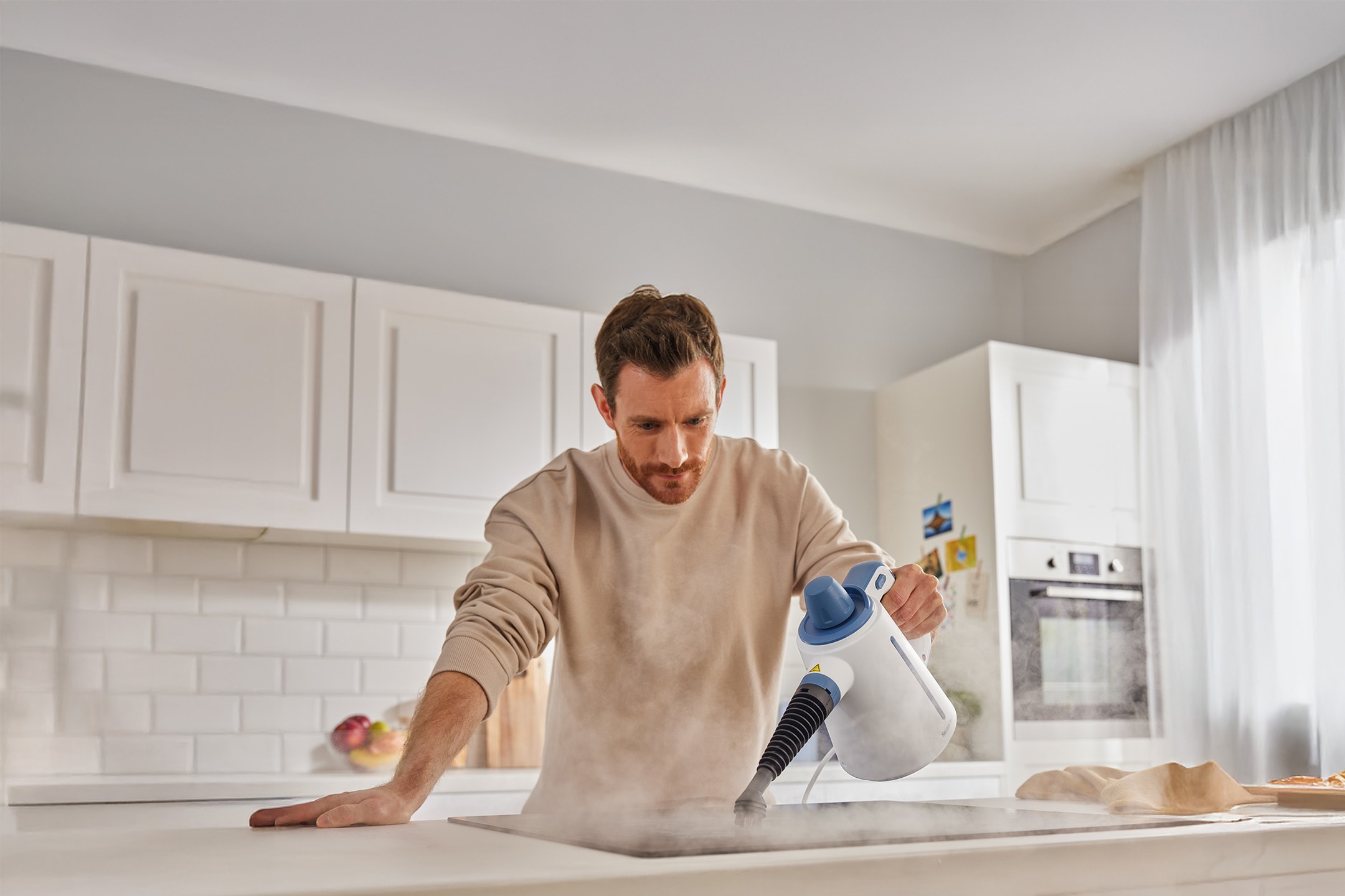 Mann reinigt Küchenkochfeld mit einem tragbaren Dampfreiniger.