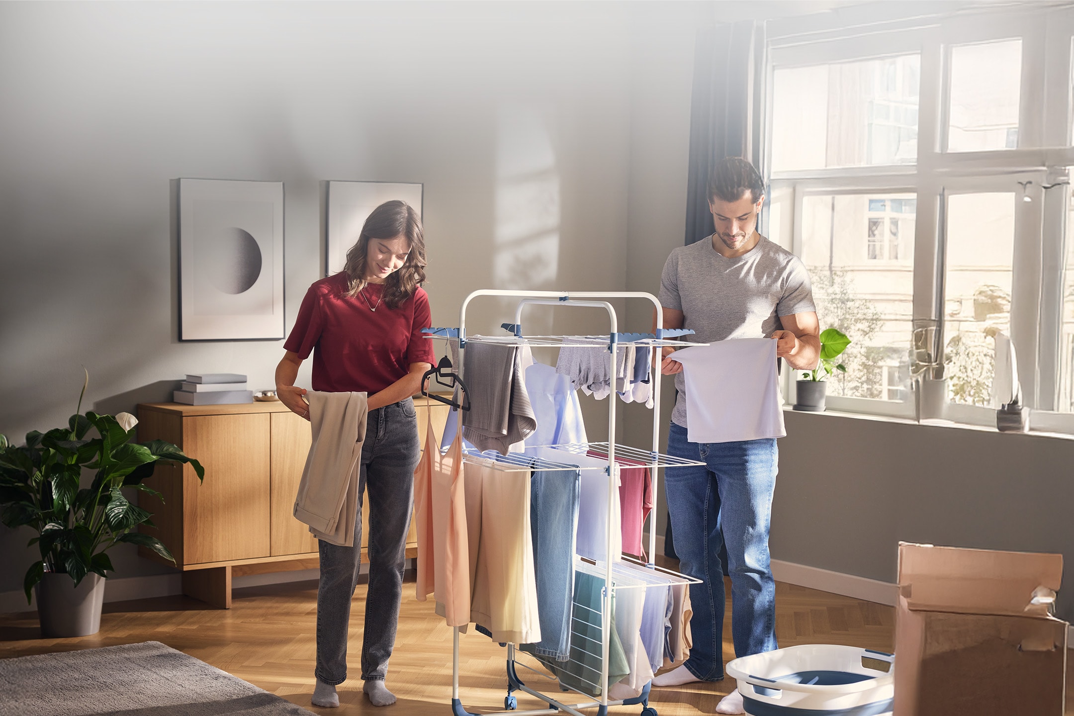 Couple étendant du linge sur un étendoir à tour dans un salon lumineux.