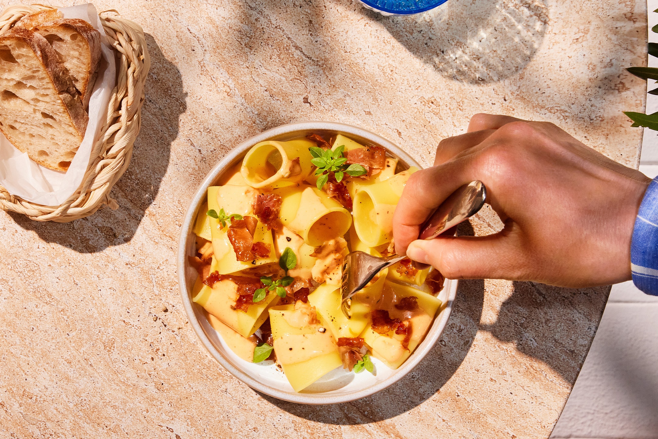 Pâtes crémeuses avec du bacon croustillant et du basilic, pain frais et eau sur une table en pierre.